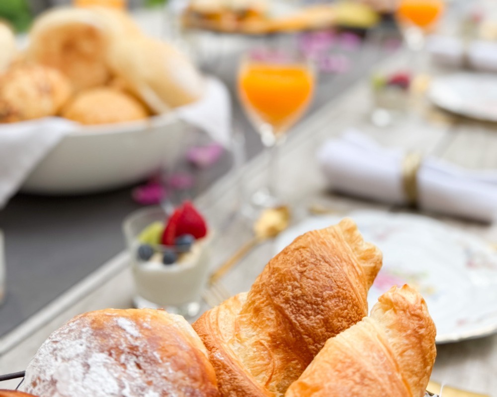 De gedekte ontbijttafel in de tuin met croissants en vers sap