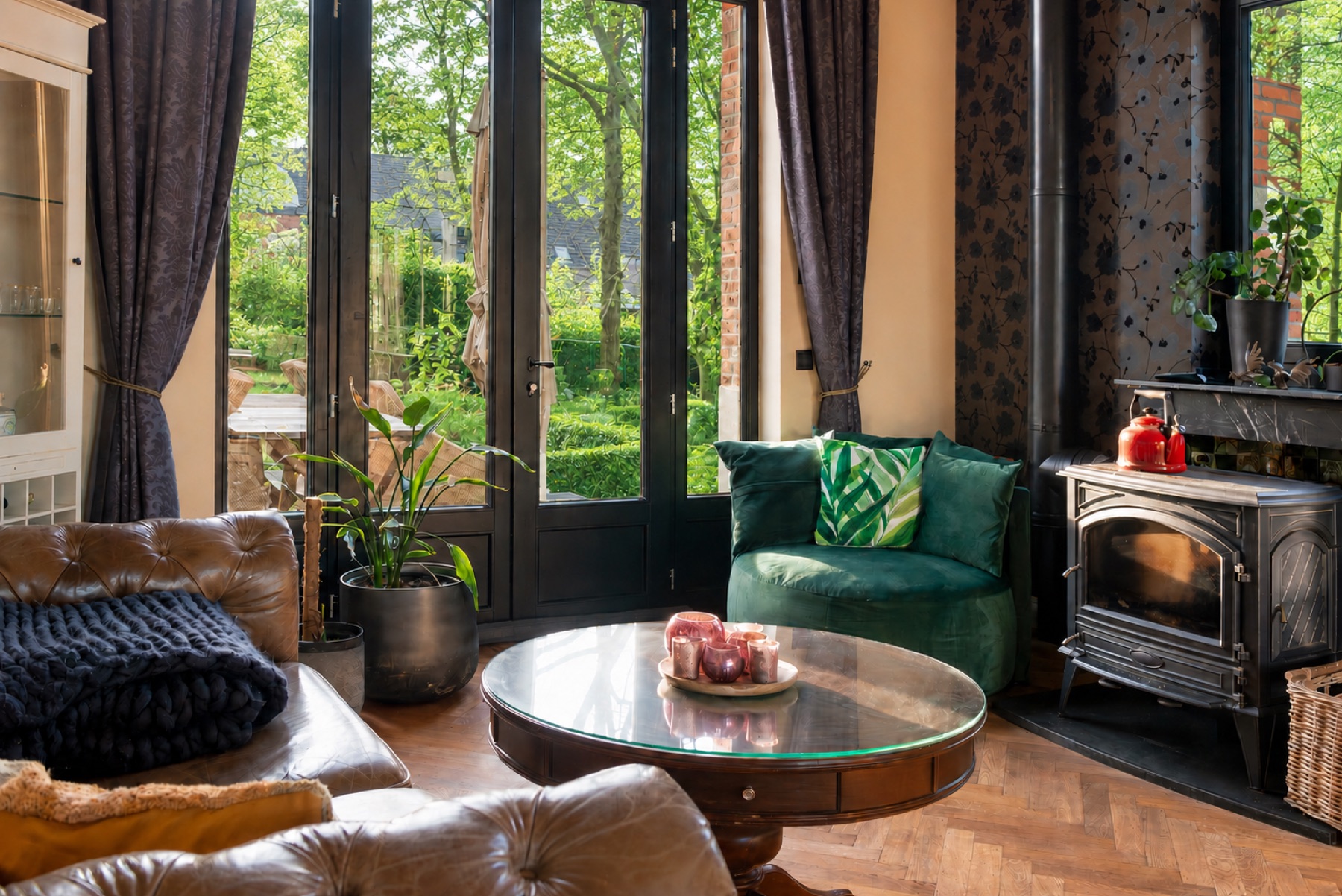 De woonkamer met leren zetel, groene fauteuil en zicht op de zomerse tuin